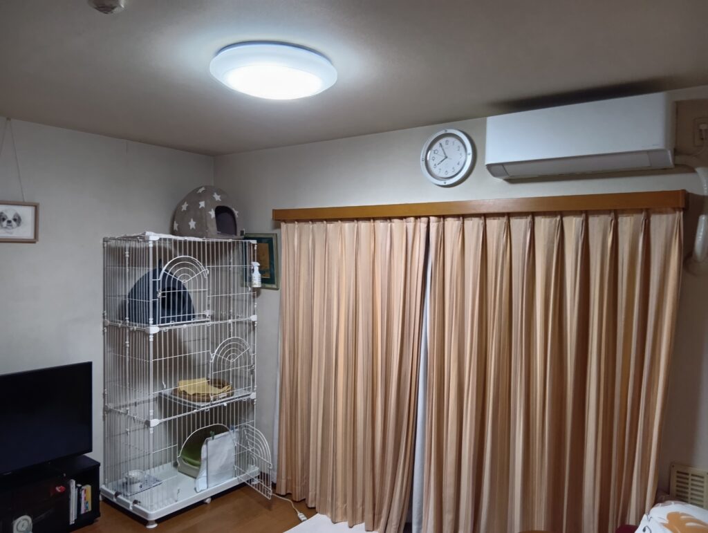 ケージとエアコンとオットーの似顔絵が飾られているリビングの写真